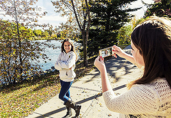 Ein Mädchen fotografiert ihre Schwester bei einem Familienausflug in einem Stadtpark an einem warmen Herbsttag: Edmonton  Alberta  Kanada