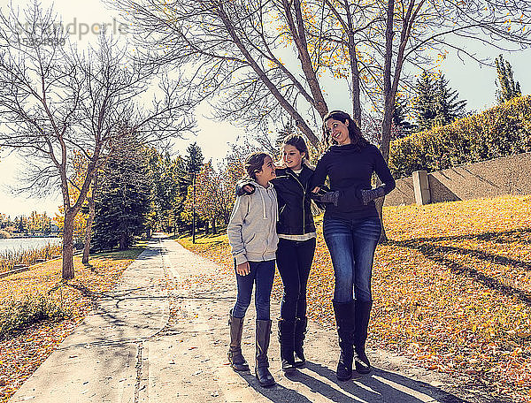 Eine Mutter und ihre beiden Töchter  die an einem warmen Herbsttag auf einem Weg in einem Stadtpark spazieren gehen und sich unterhalten; Edmonton  Alberta  Kanada