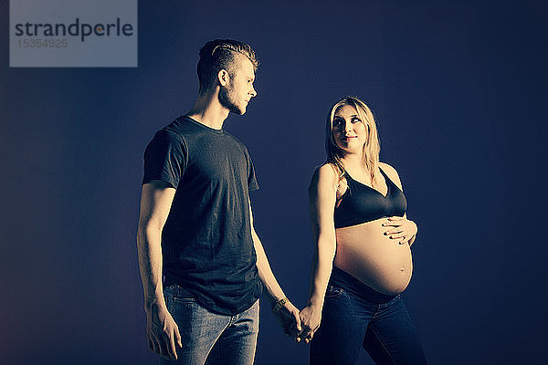Ein junges  schwangeres Paar  das sich an den Händen hält  wobei die Mutter in einem Studio auf schwarzem Hintergrund in die Kamera schaut: Edmonton  Alberta  Kanada