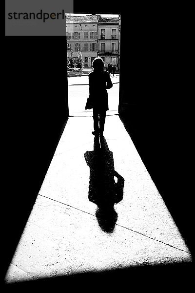 Silhouette und Schatten einer Frau  die durch ein Tor auf einem Stadtplatz in Richtung Rathaus geht; Arles  Provence Alpes Cote D'Azur  Frankreich