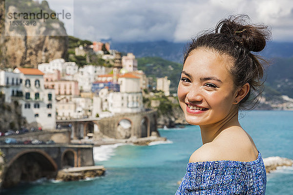 Eine junge Frau posiert mit dem Blick auf die Amalfiküste und das Mittelmeer im Hintergrund; Amalfi  Italien