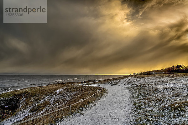 Zwei Figuren  die in der Abenddämmerung auf einem verschneiten Weg entlang der Küste spazieren gehen; South Shields  Tyne and Wear  England