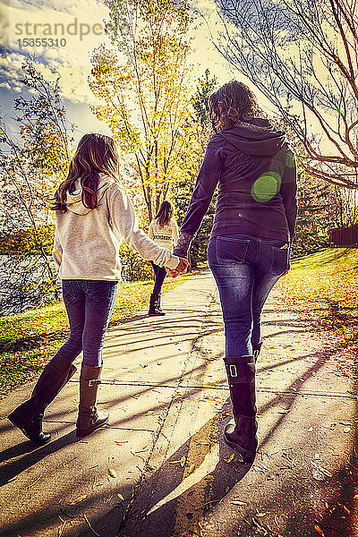 Eine Mutter und ihre beiden Töchter  die an einem warmen Herbsttag auf einem Weg in einem Stadtpark spazieren gehen und sich unterhalten; Edmonton  Alberta  Kanada