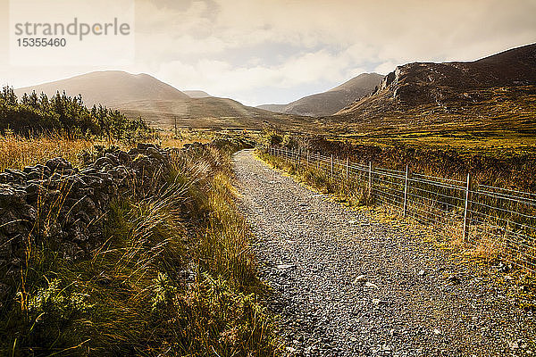 Ein Schotterweg führt bei Sonnenaufgang durch eine bergige Landschaft  Brandy Pad  Mourne Wall  Spellack  County Down  Irland