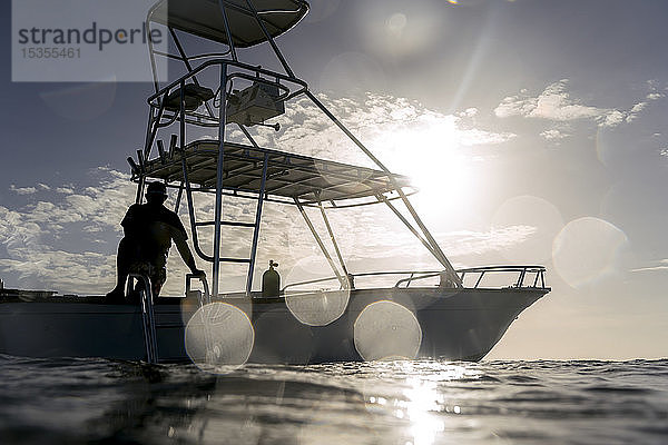 Silhouette eines Mannes auf dem Deck eines Bootes auf dem Wasser gegen einen blauen Himmel mit Sonnenlicht; Bay Islands Department  Honduras