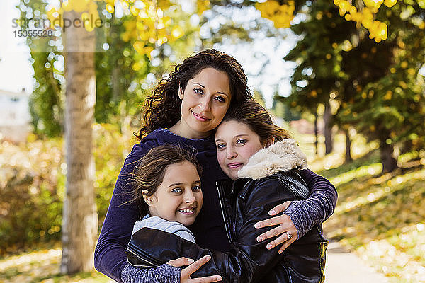 Eine Mutter und ihre beiden Töchter posieren für ein Familienporträt in einem Stadtpark an einem warmen Herbsttag; Edmonton  Alberta  Kanada