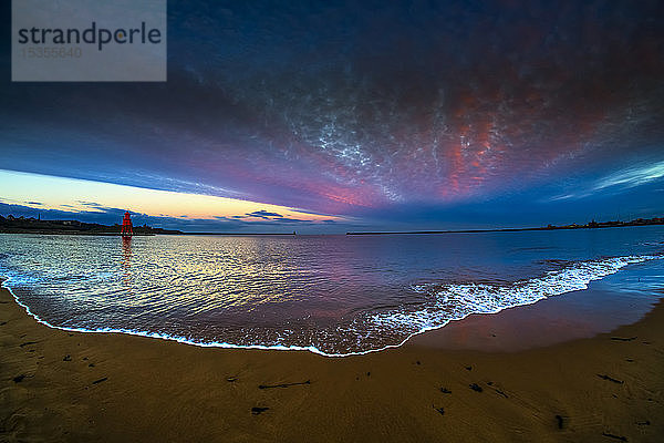 Leuchtturm Herd Groyne und dramatischer Sonnenuntergang mit leuchtenden Wolken und Flut  die im Vordergrund auf den Strand spült; South Shields  Tyne and Wear  England
