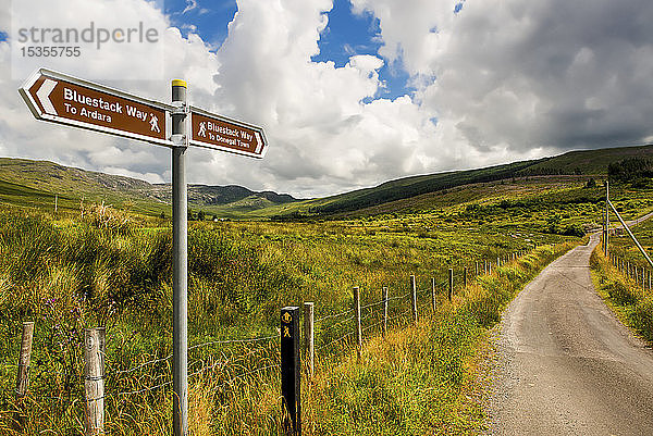 Ein Schild für Wanderwege  Bluestack Way  und eine Straße  die durch eine hügelige Landschaft führt; Grafschaft Donegal  Irland