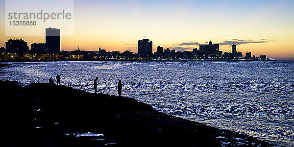 Silhouetten von Fischern entlang des Malecon mit einer Silhouette der Skyline in der Abenddämmerung; Havanna  Kuba