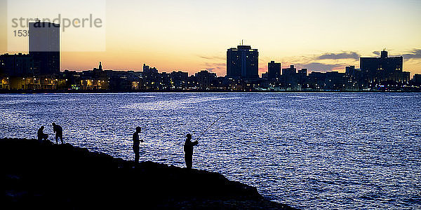 Silhouetten von Fischern entlang des Malecon mit einer Silhouette der Skyline in der Abenddämmerung; Havanna  Kuba