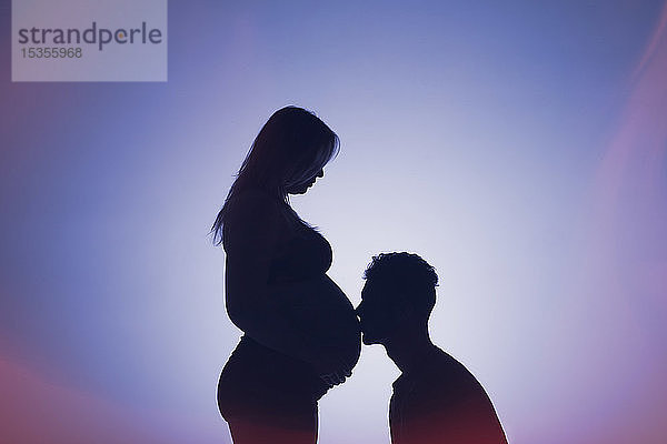 Eine Silhouette in einem Studio eines Paares  das ein Baby bekommt  wobei der Vater den Bauch der Mutter küsst  die schon weit in der Schwangerschaft ist; Edmonton  Alberta  Kanada