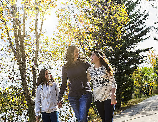 Eine Mutter und ihre beiden Töchter  die an einem warmen Herbsttag auf einem Weg in einem Stadtpark spazieren gehen und sich unterhalten; Edmonton  Alberta  Kanada