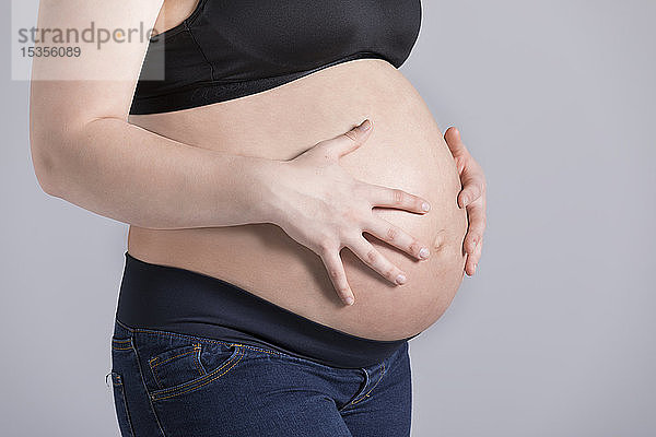 Eine junge schwangere Frau hält ihren Bauch in einem Studio vor einem hellen Hintergrund; Edmonton  Alberta  Kanada