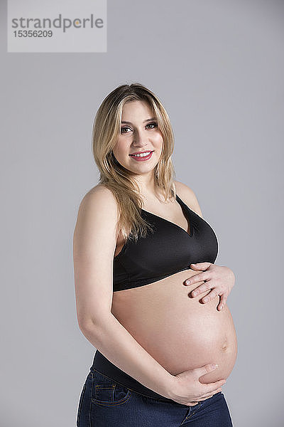 Eine junge schwangere Frau hält ihren Bauch in einem Studio und posiert für die Kamera; Edmonton  Alberta  Kanada