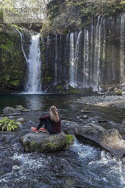 Junge Frau sitzt auf einem Stein in einem Fluss  Shiraito-Wasserfall  Präfektur Yamanashi  Japan  Asien