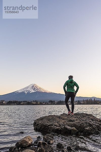 Abendstimmung  Junge Frau steht auf einem Stein im Wasser und schaut in die Ferne  Blick über den Kawaguchi-See  hinterer Vulkan Mt. Fuji  Präfektur Yamanashi  Japan  Asien