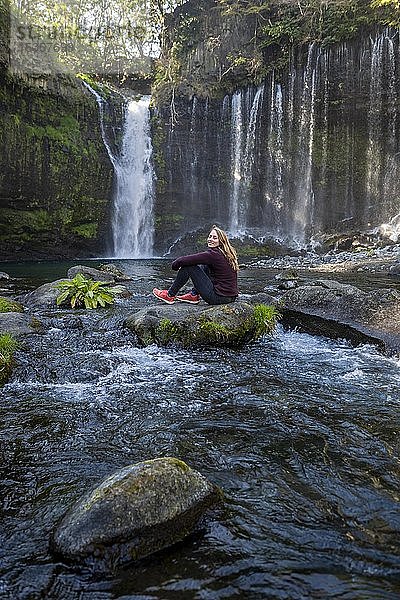 Junge Frau sitzt auf einem Stein in einem Fluss  Shiraito-Wasserfall  Präfektur Yamanashi  Japan  Asien