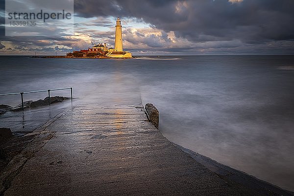 Leuchtturm  St. Mary's Lighthouse mit überspülter Straße bei Flut mit dramatischen Wolken bei Sonnenuntergang  Küste von Tyne  Northumberland  Großbritannien