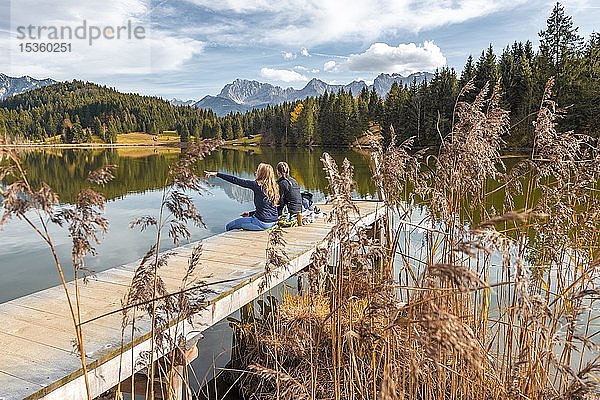 Zwei junge Frauen sitzen an einem Steg und essen eine Kleinigkeit  Geroldsee  Mittenwald  Karwendel  Bayern  Deutschland  Europa