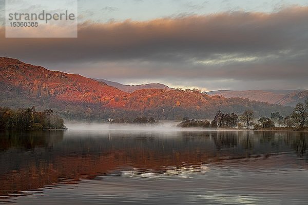 Reflektierende Wasseroberfläche bei Sonnenaufgang mit Nebel  hügelige Landschaft  Rydal Water  Ambleside  Lake District National Park  Mittelengland  Großbritannien