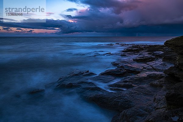 Felsige Küste mit dramatischen dunklen Wolken bei Sonnenuntergang  Newcastle upon Tyne  Northumberland  Großbritannien