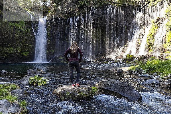 Junge Frau steht auf einem Stein in einem Fluss  Shiraito-Wasserfall  Präfektur Yamanashi  Japan  Asien