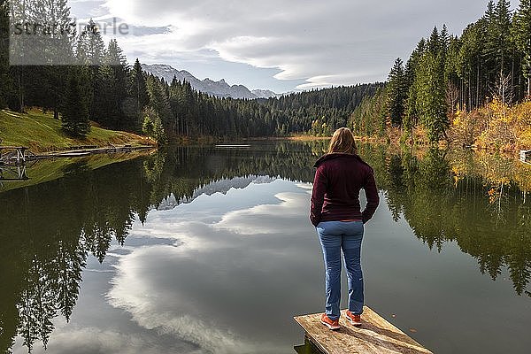 Wanderin steht auf einem Steg und schaut über den See  Herbst am Grubsee  bei Krün  Karwendel  Oberbayern  Bayern  Deutschland  Europa