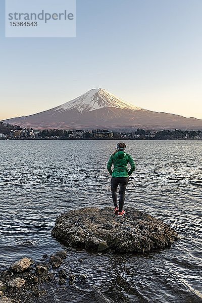 Abendstimmung  Junge Frau steht auf einem Stein im Wasser und schaut in die Ferne  Blick über den Kawaguchi-See  hinterer Vulkan Mt. Fuji  Präfektur Yamanashi  Japan  Asien