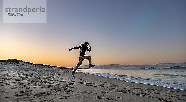 Junger Mann springt in die Luft  Strand Waipu Beach bei Sonnenuntergang  Waipu Cove  Northland  Neuseeland  Ozeanien