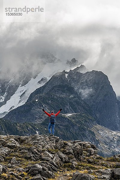Wanderin streckt die Arme in die Luft  Blick auf Mt. Shuksan mit Schnee und Gletscher  bewölkter Himmel  Mt. Baker-Snoqualmie National Forest  Washington  USA  Nordamerika
