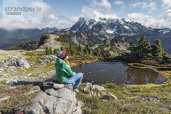 Wanderin  die sich auf einem Felsen an einem kleinen Bergsee ausruht  Blick vom Tabletop Mountain zum Mt. Shuksan mit Schnee und Gletscher  Mt. Baker-Snoqualmie National Forest  Washington  USA  Nordamerika