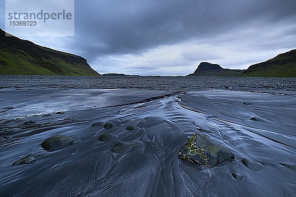 Ein kleiner Bach fließt über einen schwarzen Sandstrand ins Meer  bei Ebbe in der Talisker Bay  Isle of Skye  Schottland