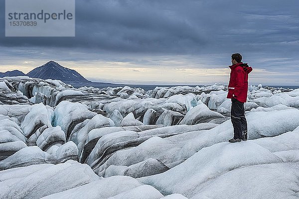 Tourist  Mann steht auf dem Eisfall eines riesigen Gletschers in Hornsund  Arktis  Svalbard  Norwegen  Europa