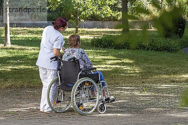 Frau sitzt im Rollstuhl  Krankenschwester geht mit Frau im Rollstuhl  Deutschland  Europa