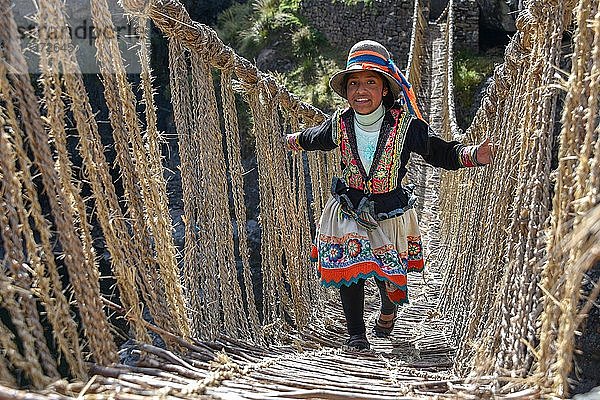 Lachendes einheimisches Mädchen in Tracht geht über die Inka-Hängebrücke Q'iswachaka  eine Seilbrücke aus geflochtenem Ichu-Gras über den Fluss Apurimac  Provinz Canas  Peru  Südamerika