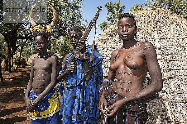 Junge Mädchen mit Schmucknarben und Mann mit Kalaschnikow vor einer Hütte  Stamm der Mursi  Mago-Nationalpark  Region der südlichen Nationen und Völker  Äthiopien  Afrika