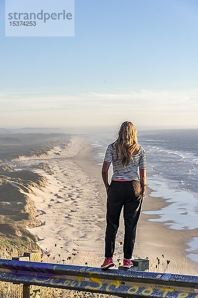 Junge Frau schaut an einem Aussichtspunkt in die Ferne  Blick über Baker Beach mit langem Sandstrand  Oregon Coast Highway  Oregon  USA  Nordamerika
