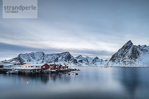 Rorbuerhütten von Hamnoy in der blauen Stunde  hinter schneebedeckten Bergen  Olstinden  Hamnøy  Moskenesøya  Lofoten  Norwegen  Europa