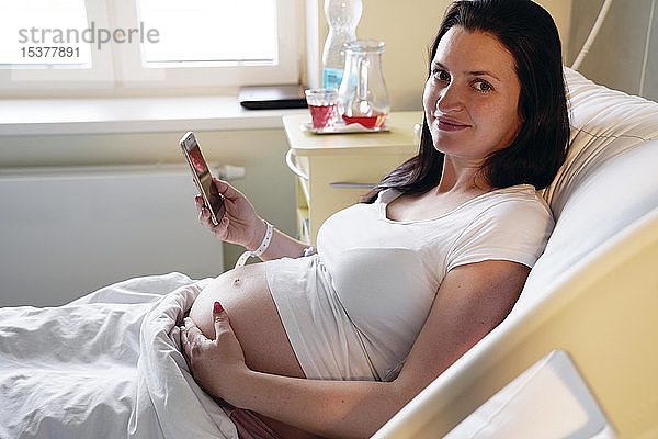 Risikoschwangerschaft  schwangere Frau im Krankenhaus auf dem Entbindungsbett liegend mit Handy  Karlovy Vary  Tschechische Republik  Europa