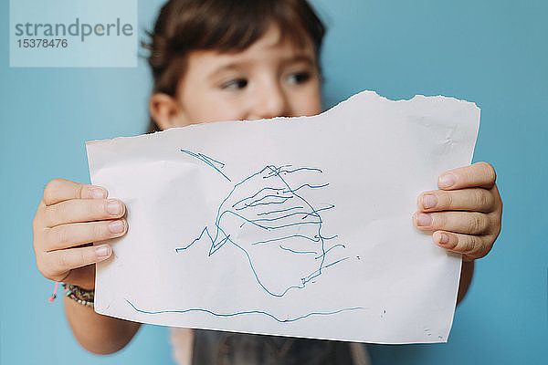 Kleines Mädchen hält eine handgemachte Zeichnung auf blauem Hintergrund