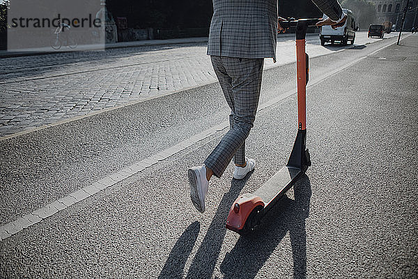 Geschäftsmann zu Fuß mit E-Scooter in der Stadt