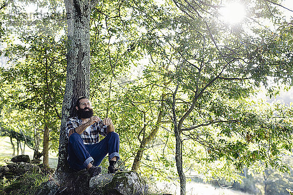 Mann mit Bart entspannt sich am Baumstamm im Wald