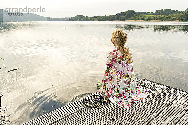 Junge Frau sitzt auf einem Steg an einem See