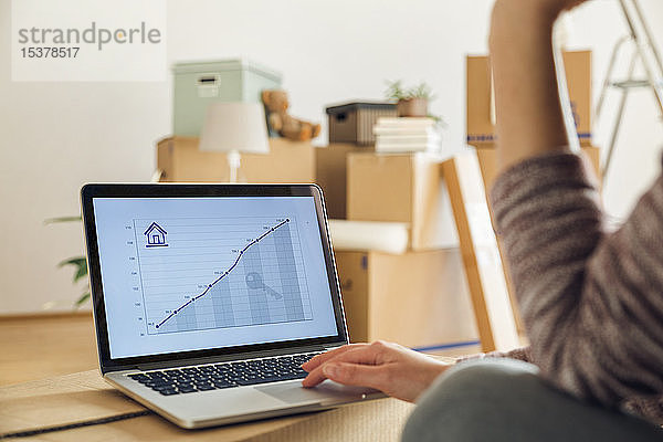 Frau mit Laptop mit aufsteigender Liniengrafik auf dem Bildschirm in einem neuen Zuhause