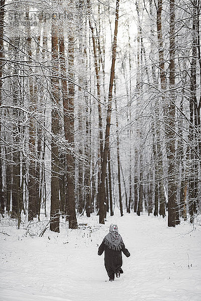 Rückenansicht eines kleinen Mädchens mit Kopftuch beim Spaziergang im Winterwald