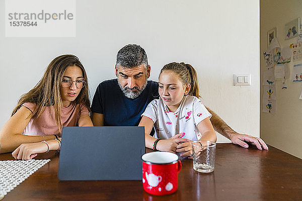 Vater mit zwei Töchtern betrachtet Tafel auf Holztisch zu Hause