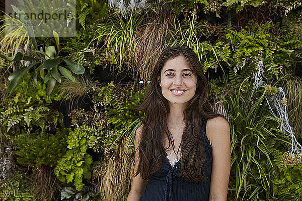 Porträt einer lächelnden jungen Frau vor einer Pflanzenwand