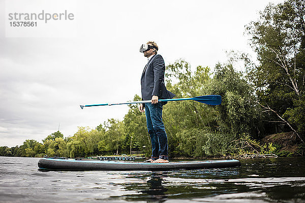 Geschäftsmann mit VR-Brille auf einem SUP-Brett auf einem See