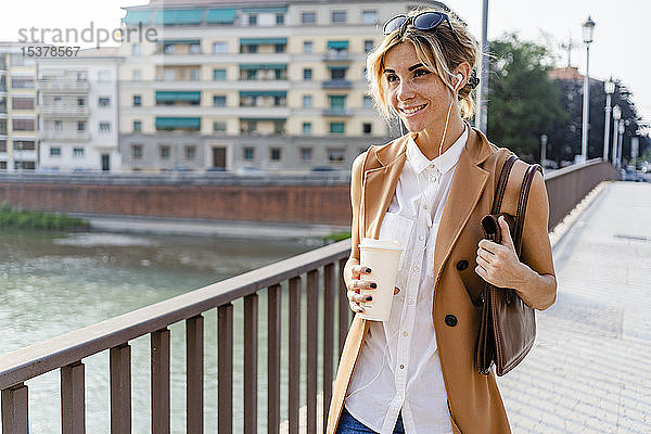 Lächelnde Frau mit Kopfhörern und Kaffee zum Stadtbummel