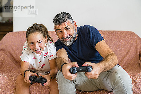 Vater und Tochter spielen zu Hause auf der Couch Videospiele